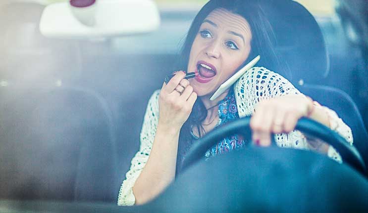 Woman driving while on phone and applying makeup